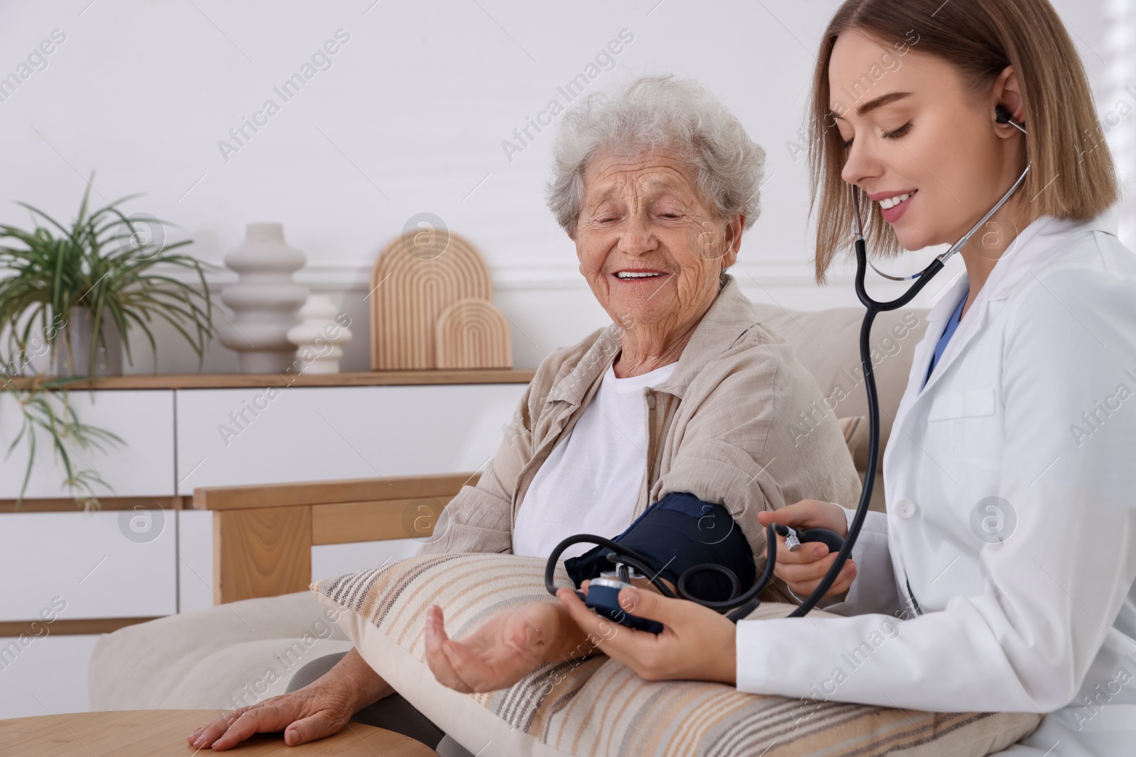 Photo of Doctor measuring patient's blood pressure on sofa indoors