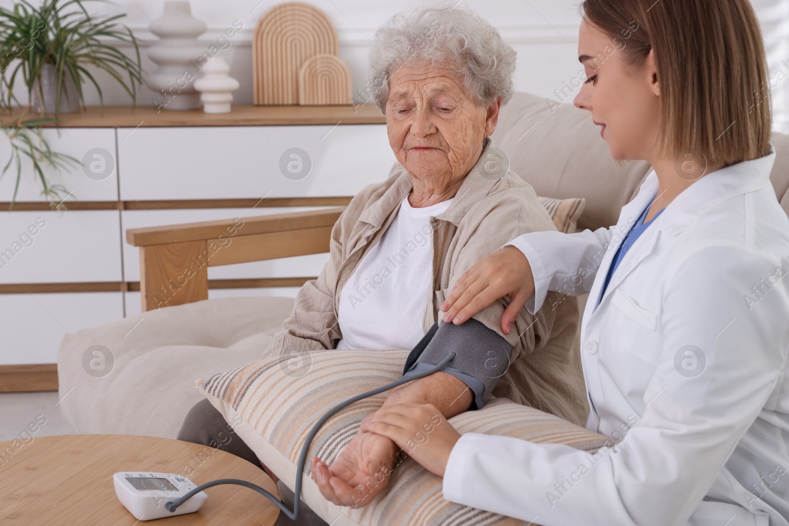 Photo of Doctor measuring patient's blood pressure on sofa indoors