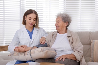 Doctor measuring patient's blood pressure on sofa indoors