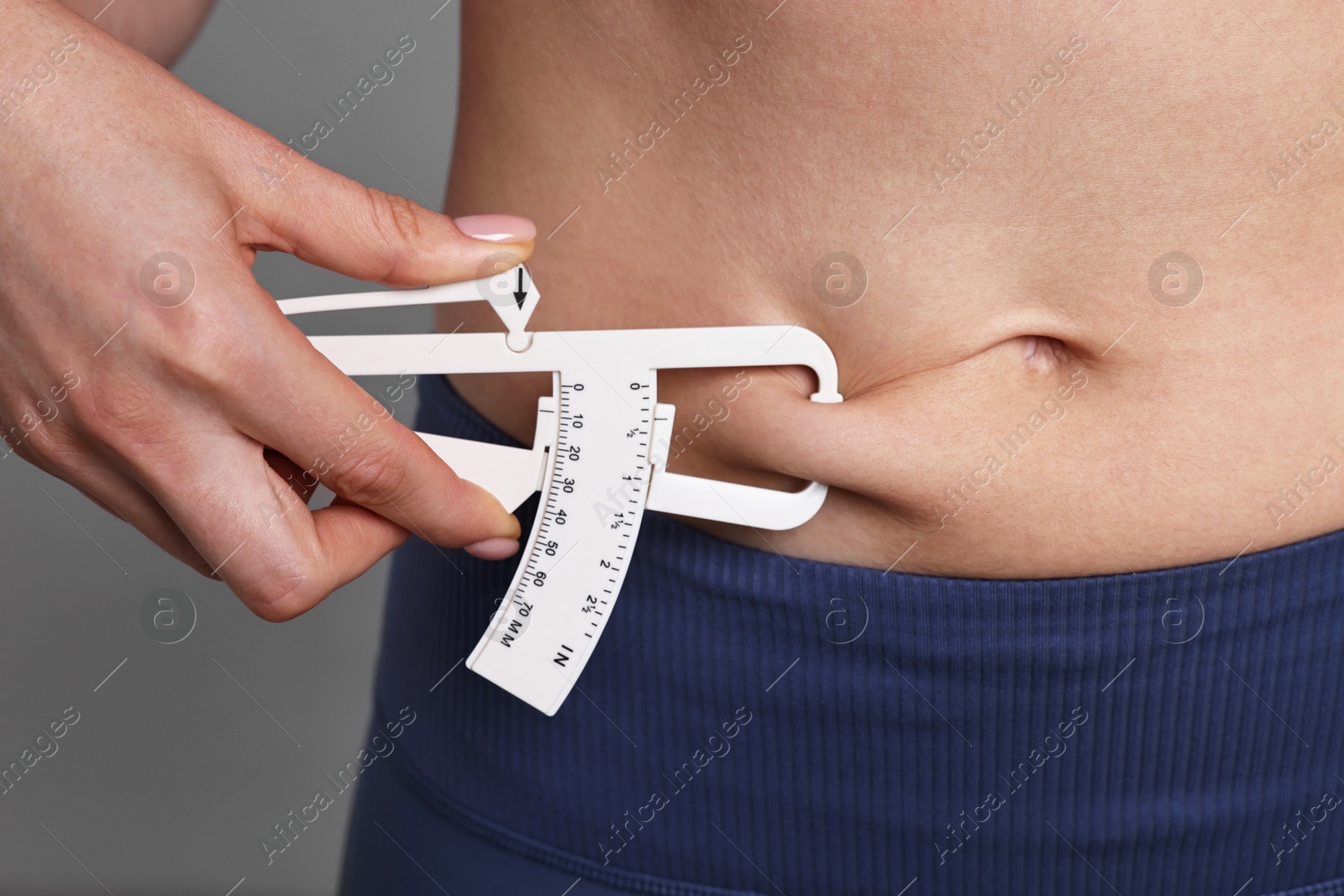 Photo of Woman measuring body fat with caliper on gray background, closeup