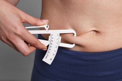 Photo of Woman measuring body fat with caliper on gray background, closeup