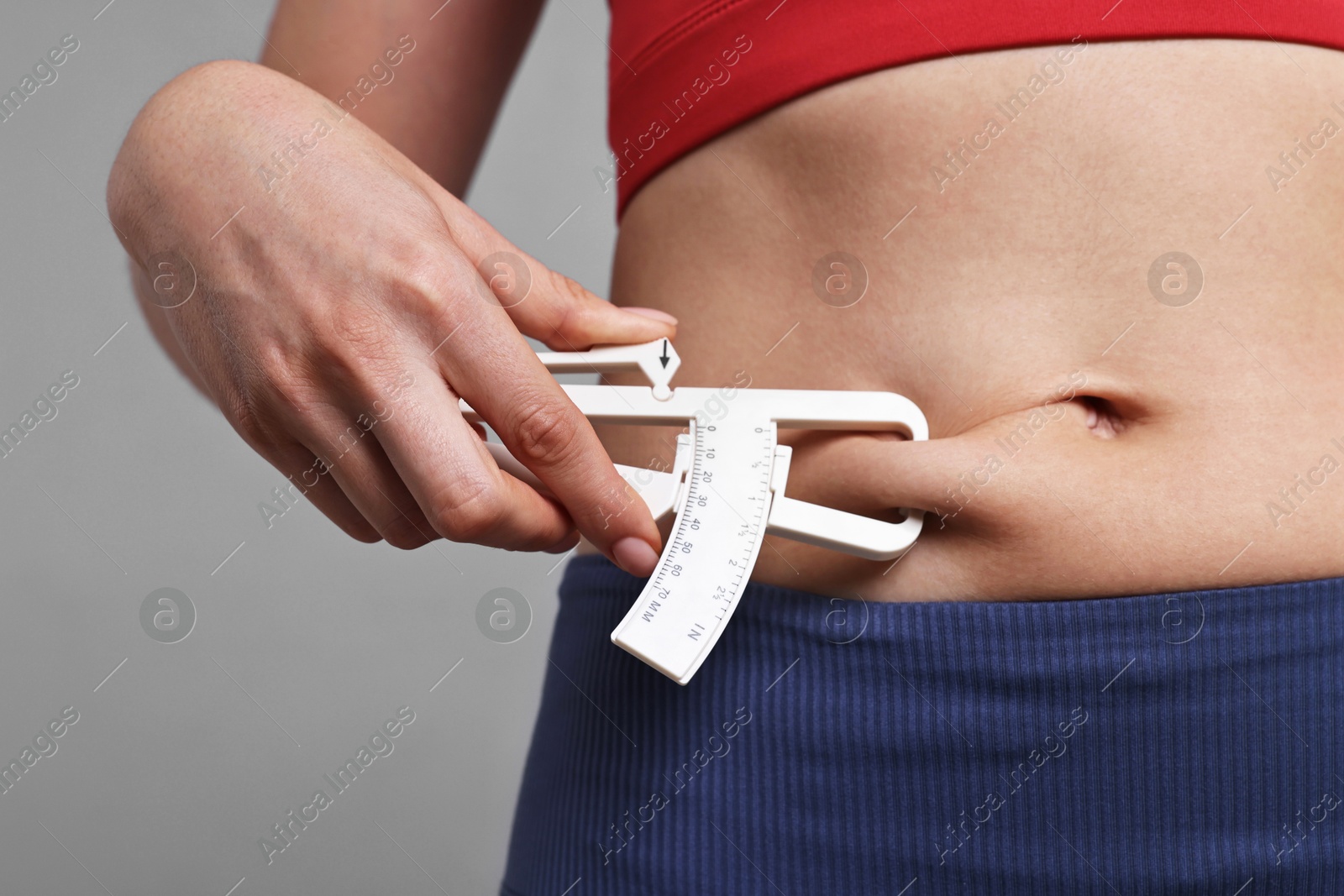 Photo of Woman measuring body fat with caliper on gray background, closeup