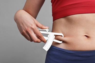 Photo of Woman measuring body fat with caliper on gray background, closeup