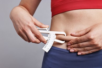 Photo of Woman measuring body fat with caliper on gray background, closeup