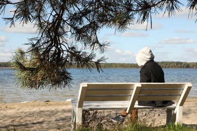 Loneliness concept. Sad man sitting on bench at riverside, selective focus