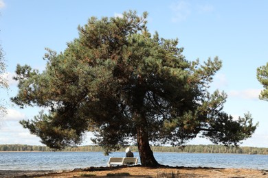 Photo of Loneliness concept. Sad man sitting on bench under tree at riverside