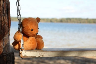 Lonely teddy bear on swing near river