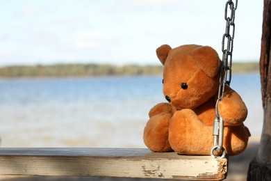 Photo of Lonely teddy bear on swing near river