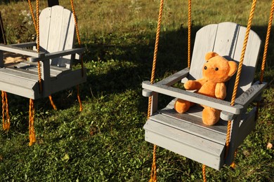 Lonely teddy bear on swing in park