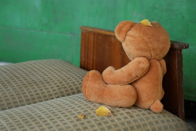 Photo of Lonely teddy bear on old bed near green wall outdoors