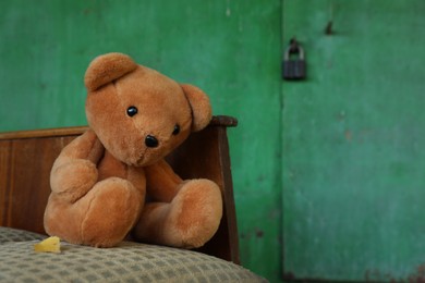 Photo of Lonely teddy bear on old bed near green wall outdoors