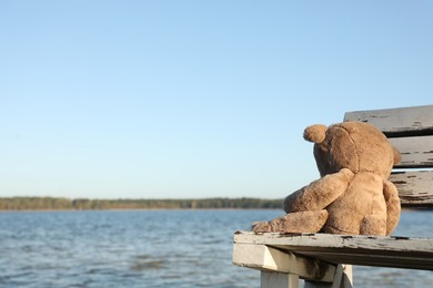 Lonely teddy bear on bench near river, space for text