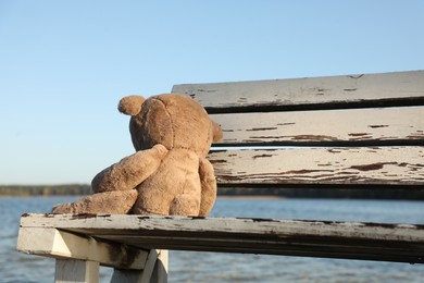 Lonely teddy bear on bench near river