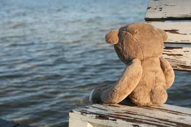 Lonely teddy bear on bench near river, space for text