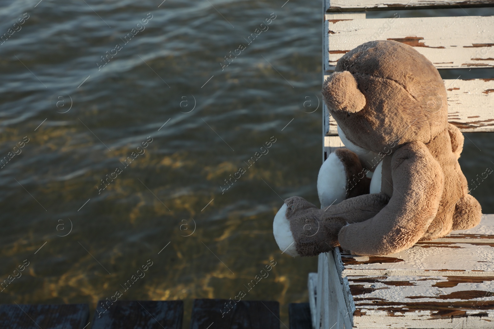 Photo of Lonely teddy bear on bench near river, space for text