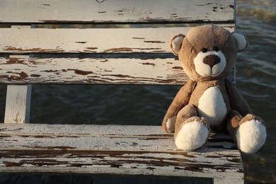 Lonely teddy bear on bench near river