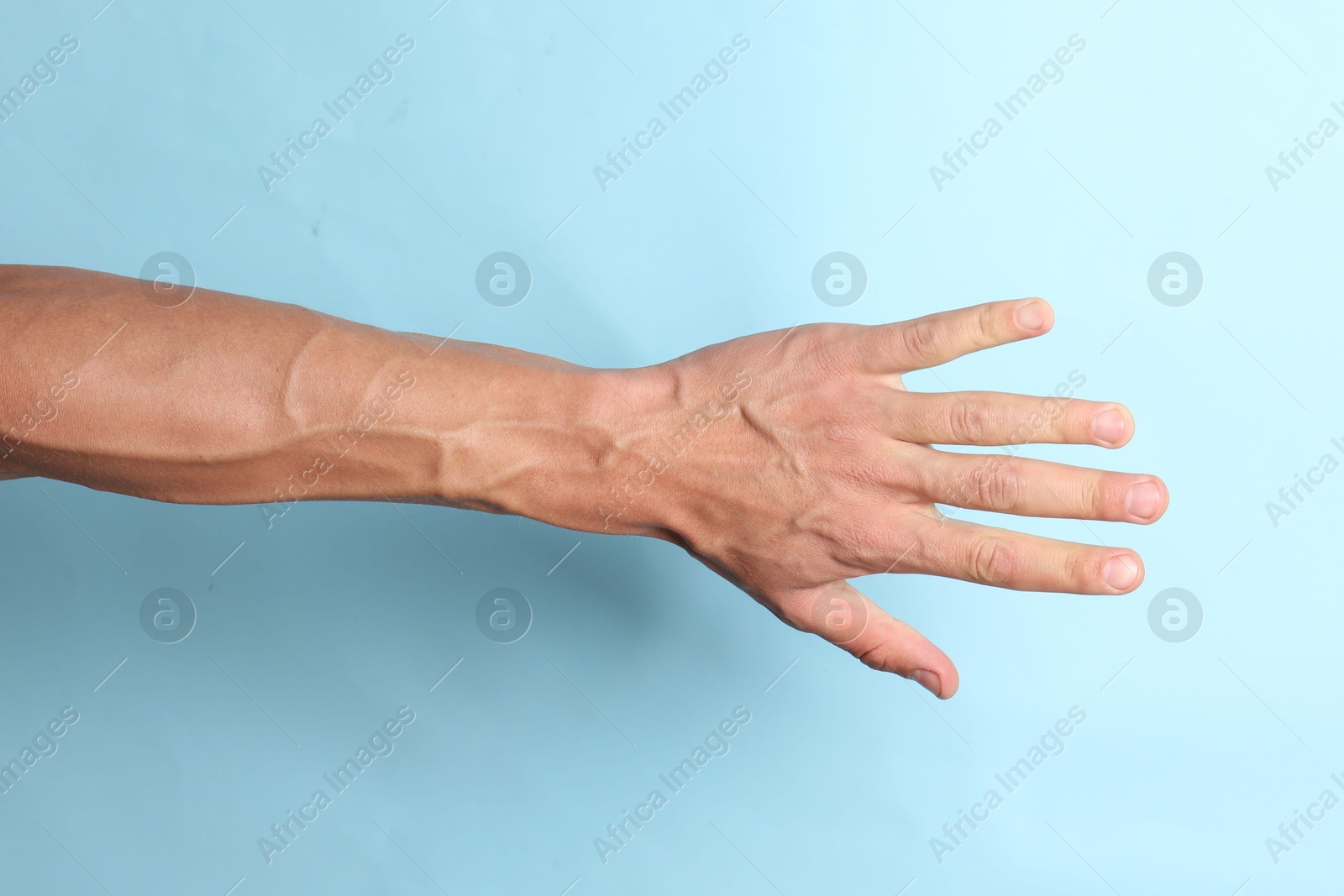 Photo of Man with bulging veins on his arm against light blue background, closeup