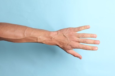 Man with bulging veins on his arm against light blue background, closeup