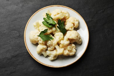 Photo of Tasty cauliflower with parsley on black table, top view