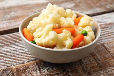 Photo of Tasty cauliflower with baby carrots and green peas on wooden table, closeup