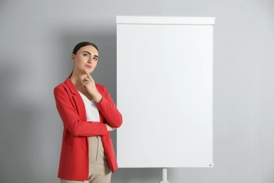 Thoughtful woman near flip chart on grey background. Mockup for design