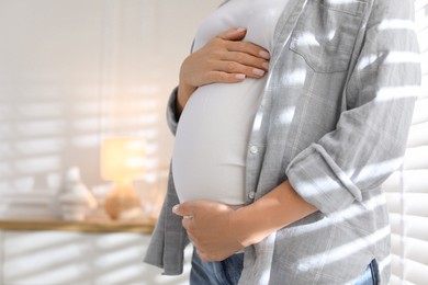 Pregnant woman near window at home, closeup. Space for text