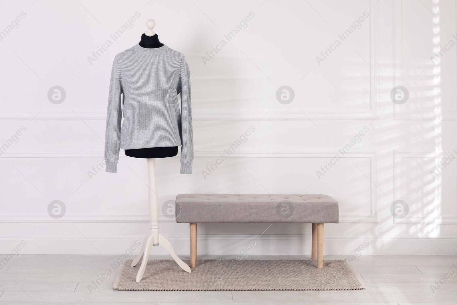 Photo of Female mannequin with sweater and bench near light wall