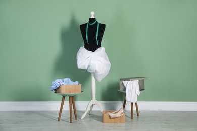 Photo of Female mannequin with fabric, measuring tape and clothes near green wall