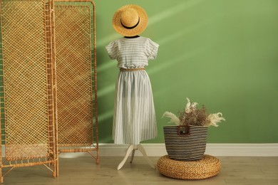 Photo of Female mannequin with dress, hat, bag, dry plants and folding screen near green wall