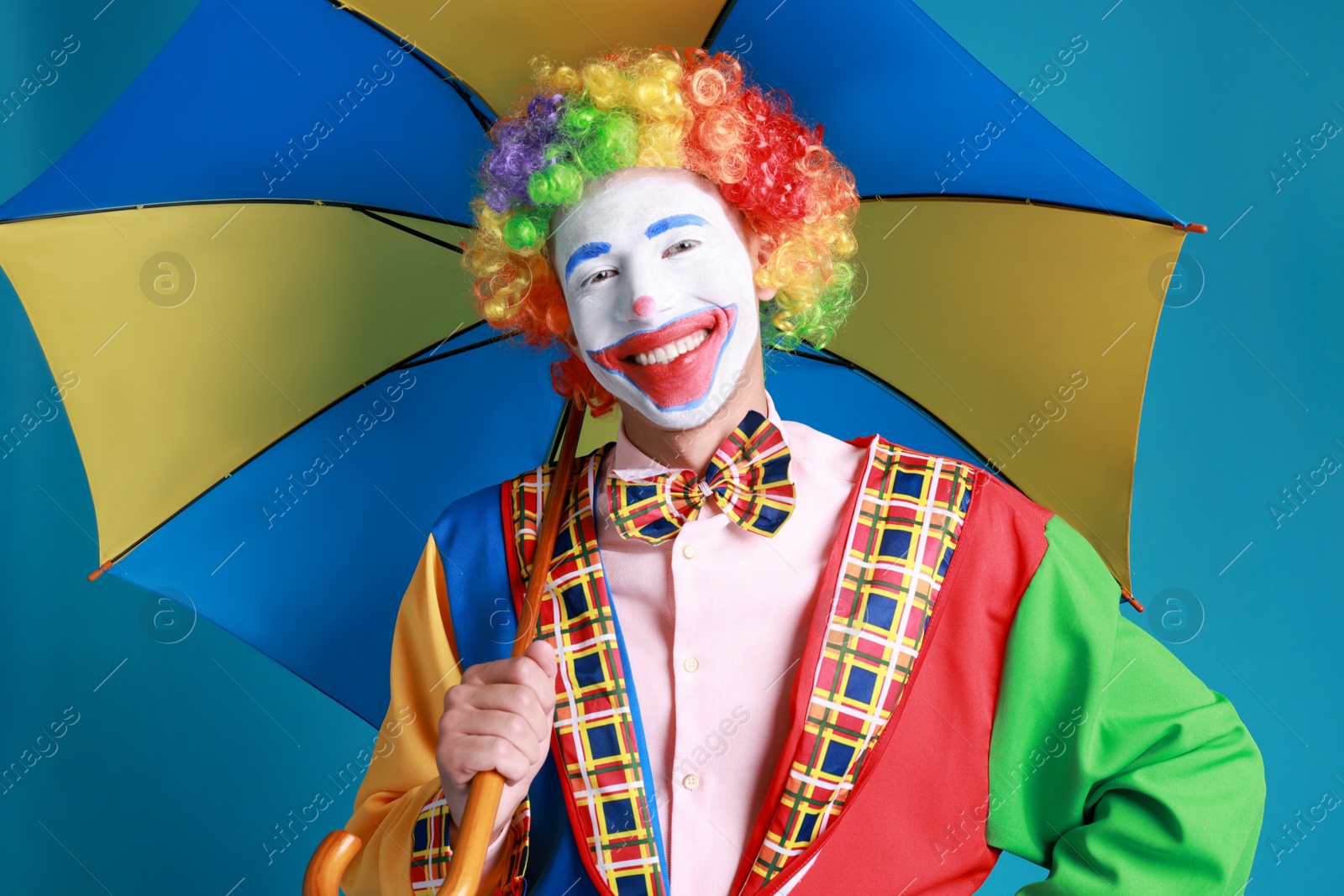 Photo of Clown with colorful umbrella on blue background