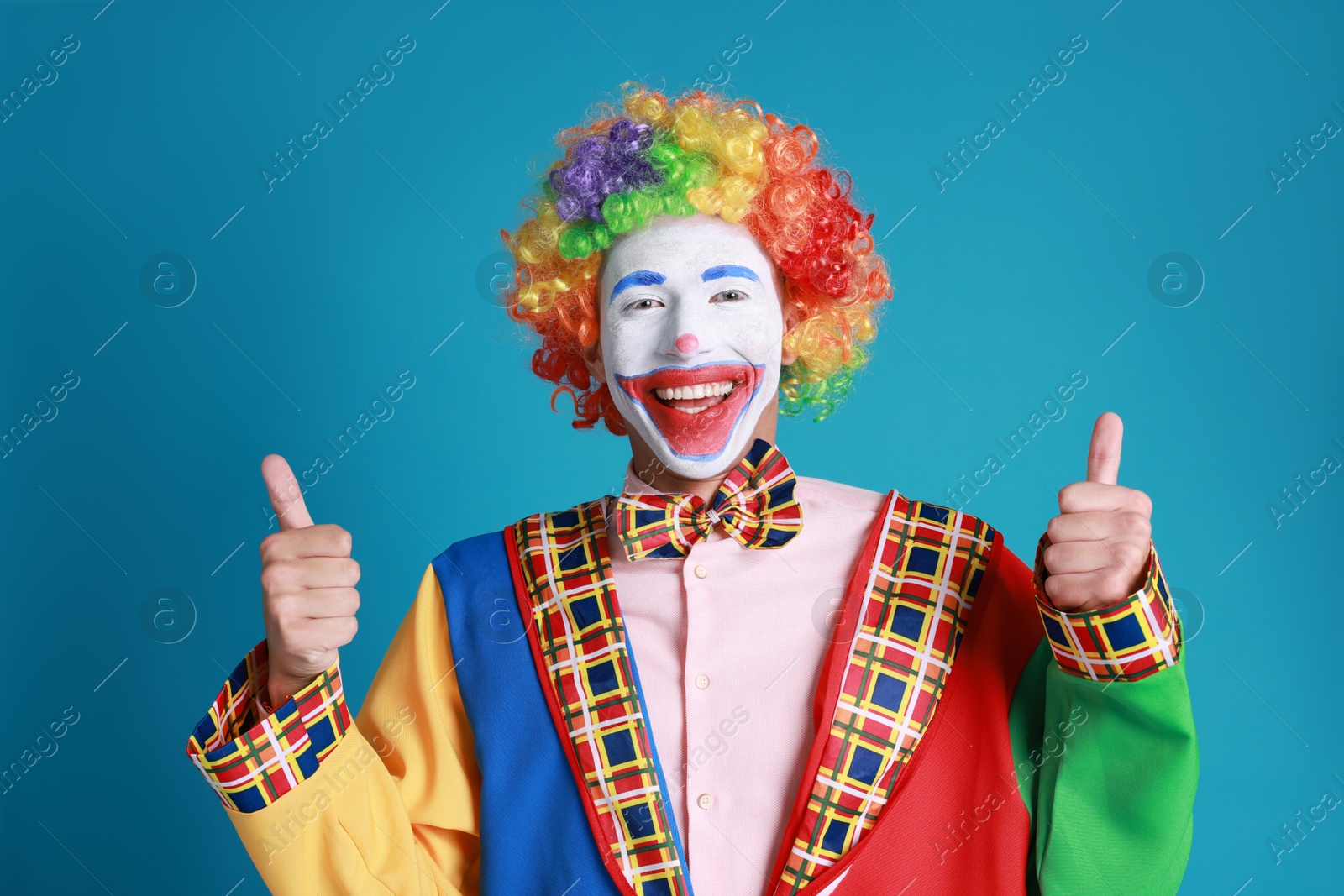 Photo of Happy clown showing thumbs up on blue background