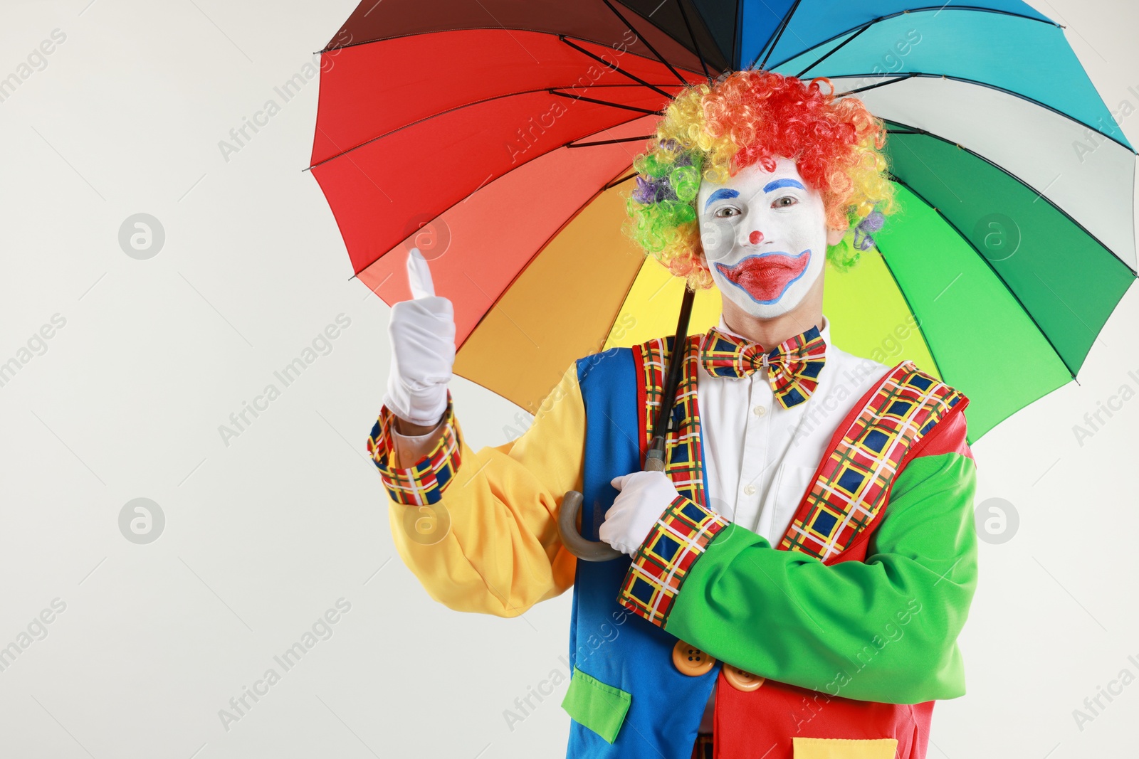 Photo of Clown with colorful umbrella showing thumbs up on light background, space for text