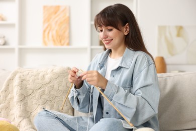 Beautiful woman knitting on sofa at home