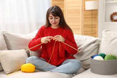 Beautiful woman knitting on sofa at home