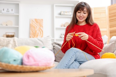 Beautiful woman knitting on sofa at home