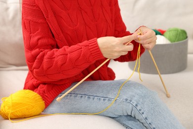 Photo of Woman knitting with needles on sofa at home, closeup