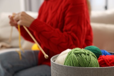 Photo of Woman knitting with needles at home, focus on colorful yarns