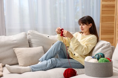 Beautiful woman knitting on sofa at home