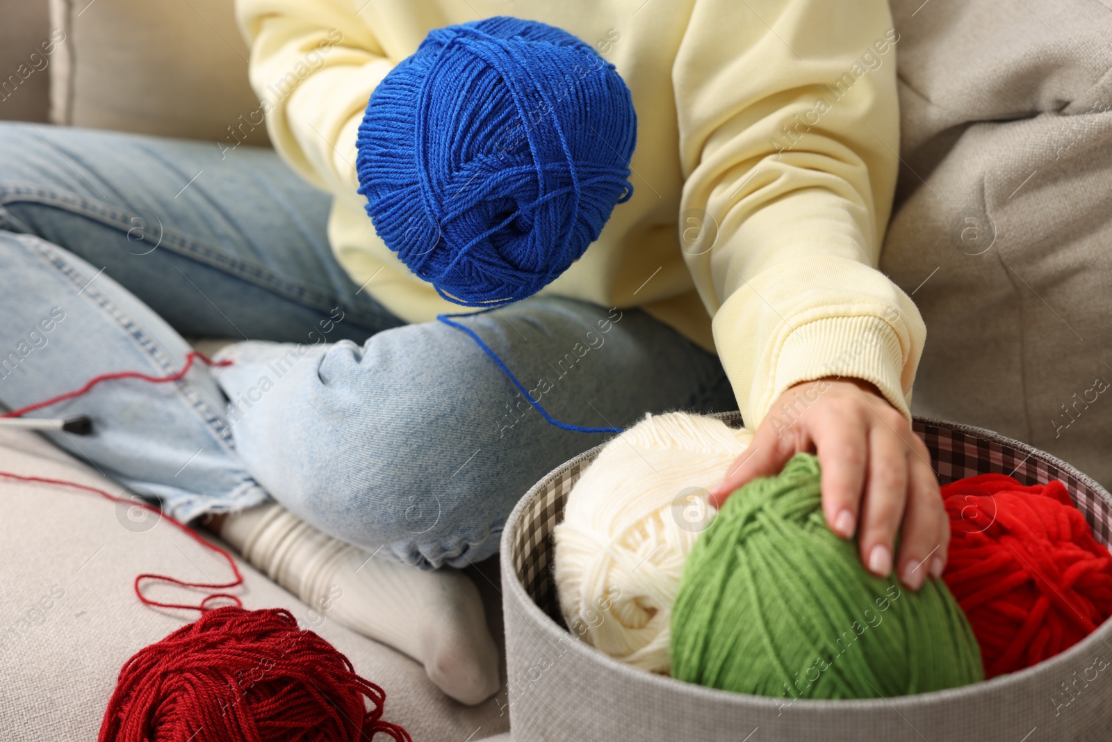 Photo of Woman with colorful yarns on sofa at home, closeup. Knitting material