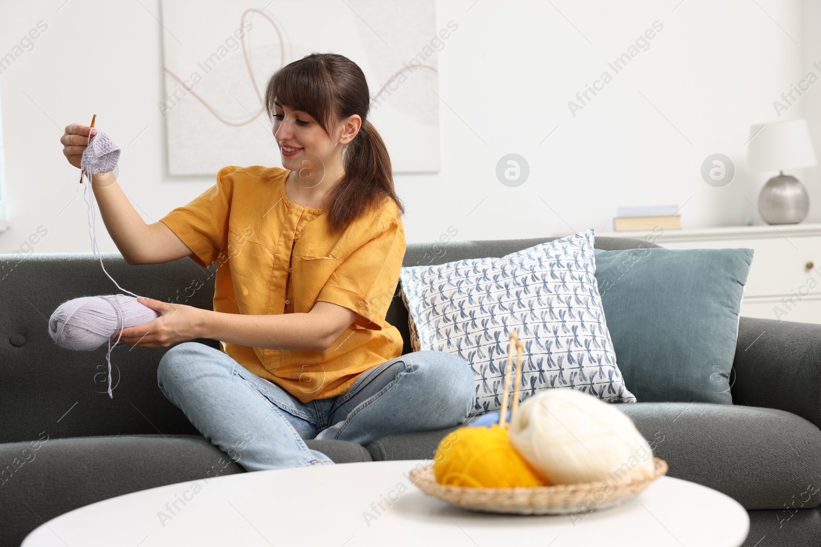 Photo of Beautiful woman crocheting with hook on sofa at home