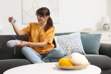 Photo of Beautiful woman crocheting with hook on sofa at home