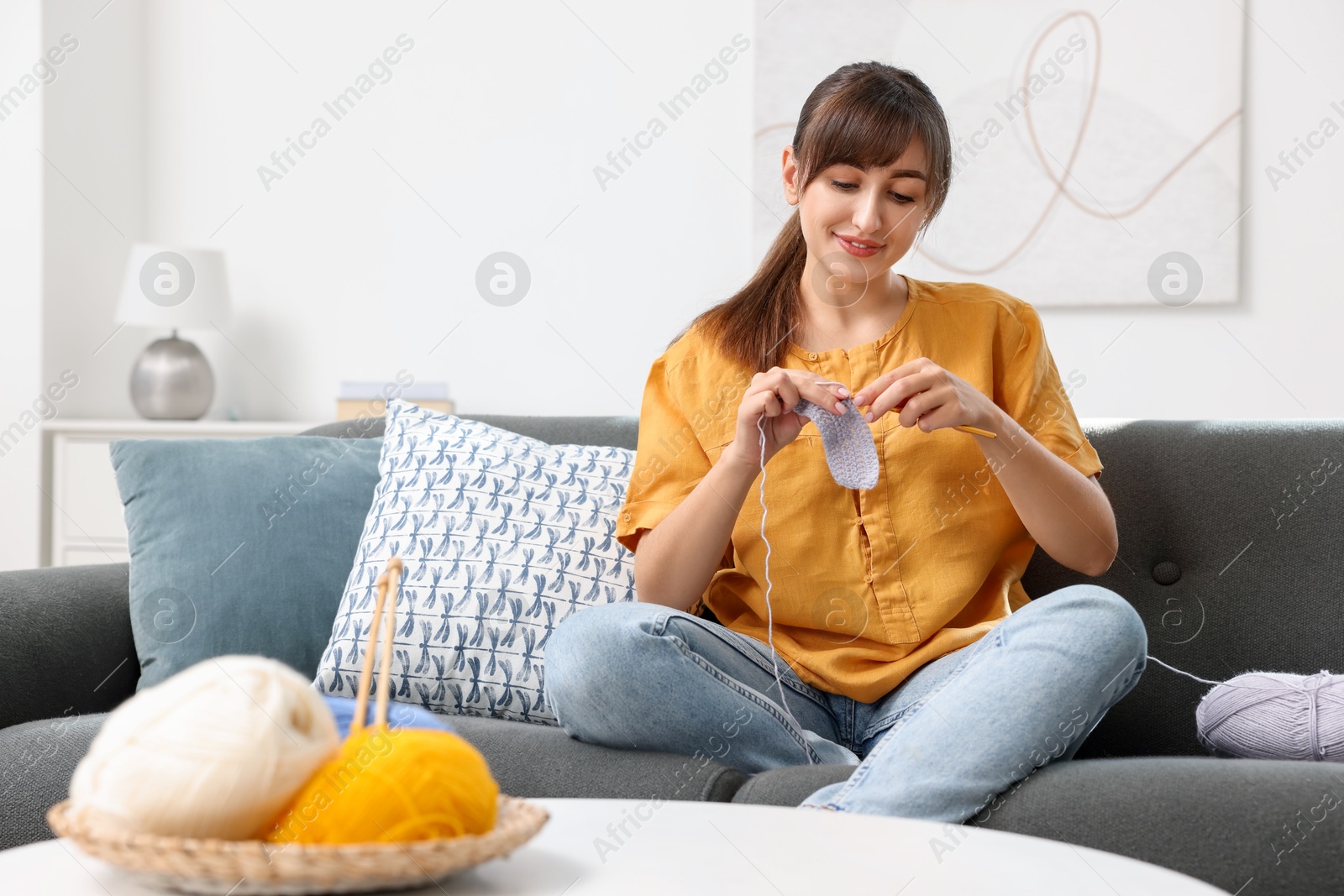 Photo of Beautiful woman crocheting with hook on sofa at home