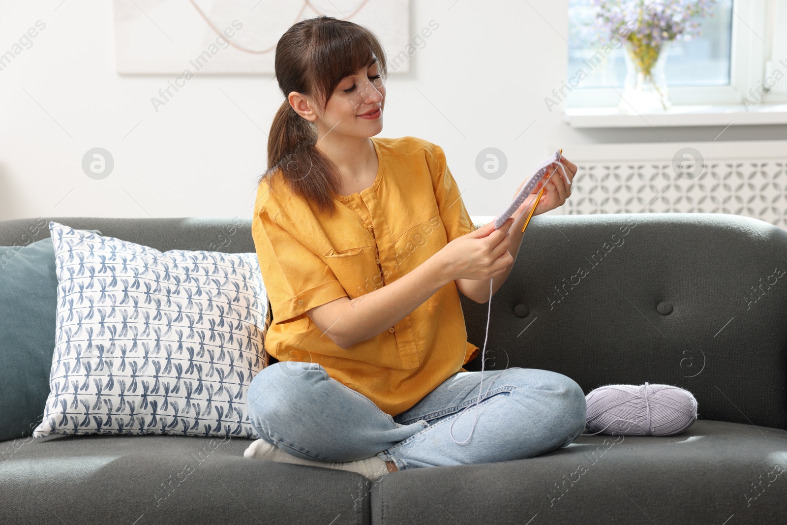 Photo of Beautiful woman crocheting with hook on sofa at home