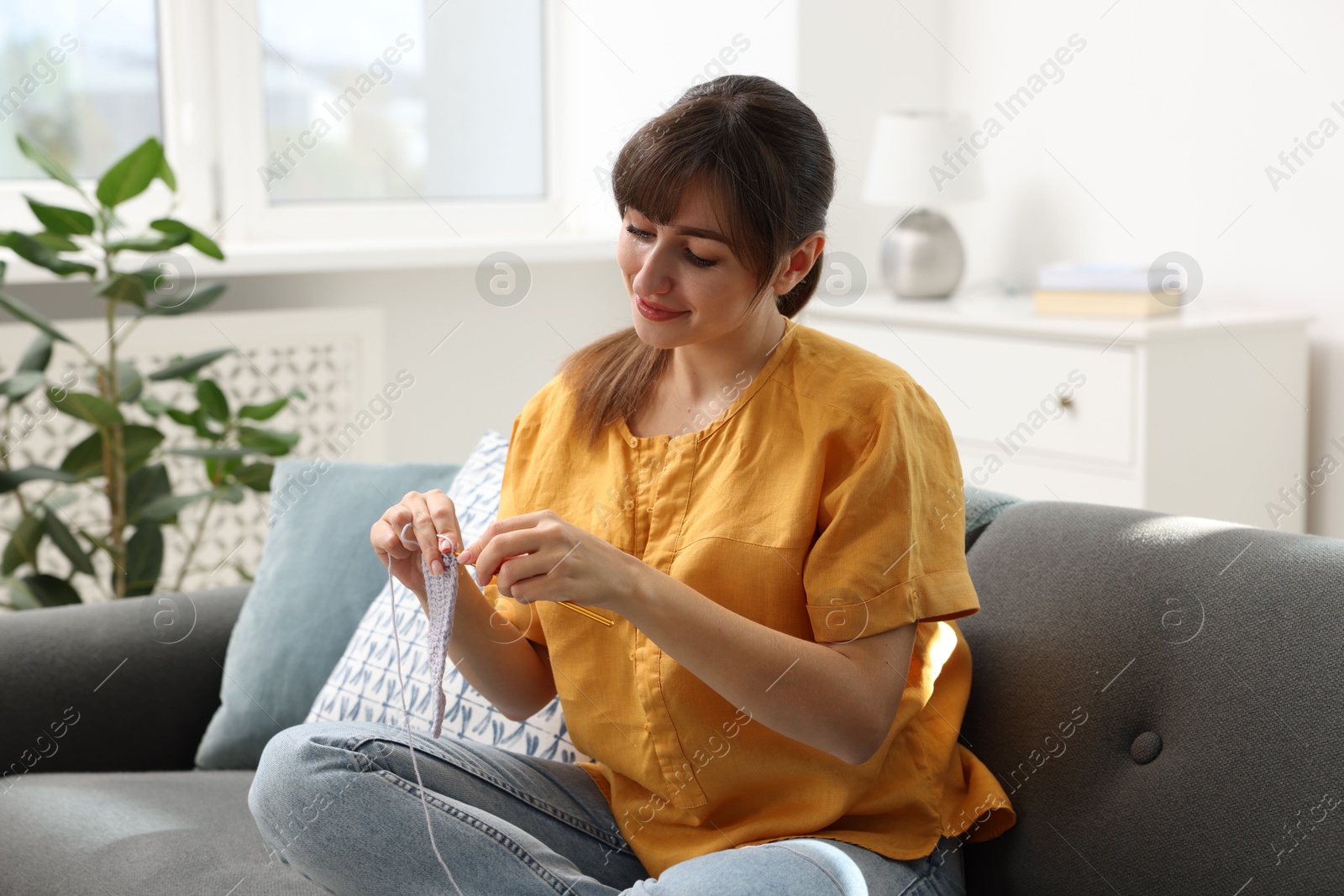 Photo of Beautiful woman crocheting with hook on sofa at home