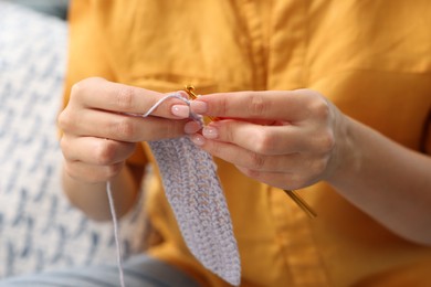 Photo of Woman crocheting with hook at home, closeup