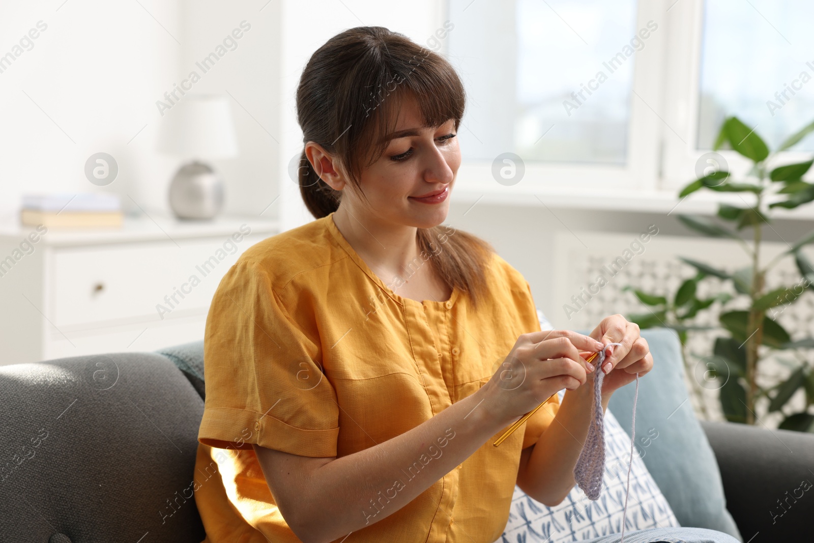 Photo of Beautiful woman crocheting with hook on sofa at home