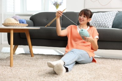 Beautiful woman knitting with needles on floor at home