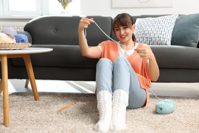 Photo of Beautiful woman knitting with needles on floor at home