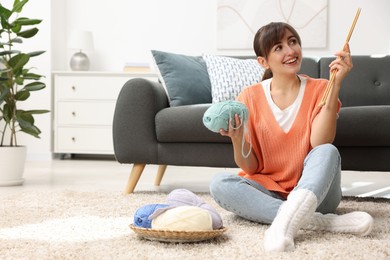 Beautiful woman with colorful yarns and knitting needles on floor at home