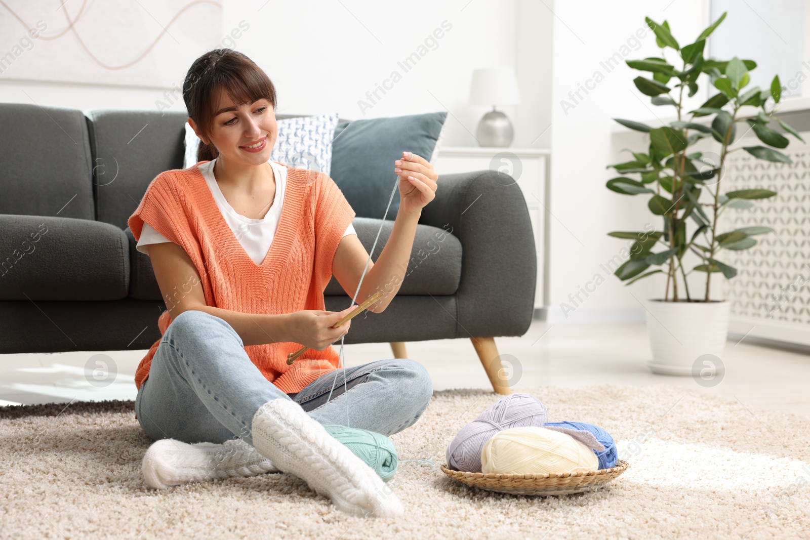 Photo of Beautiful woman knitting with needles on floor at home